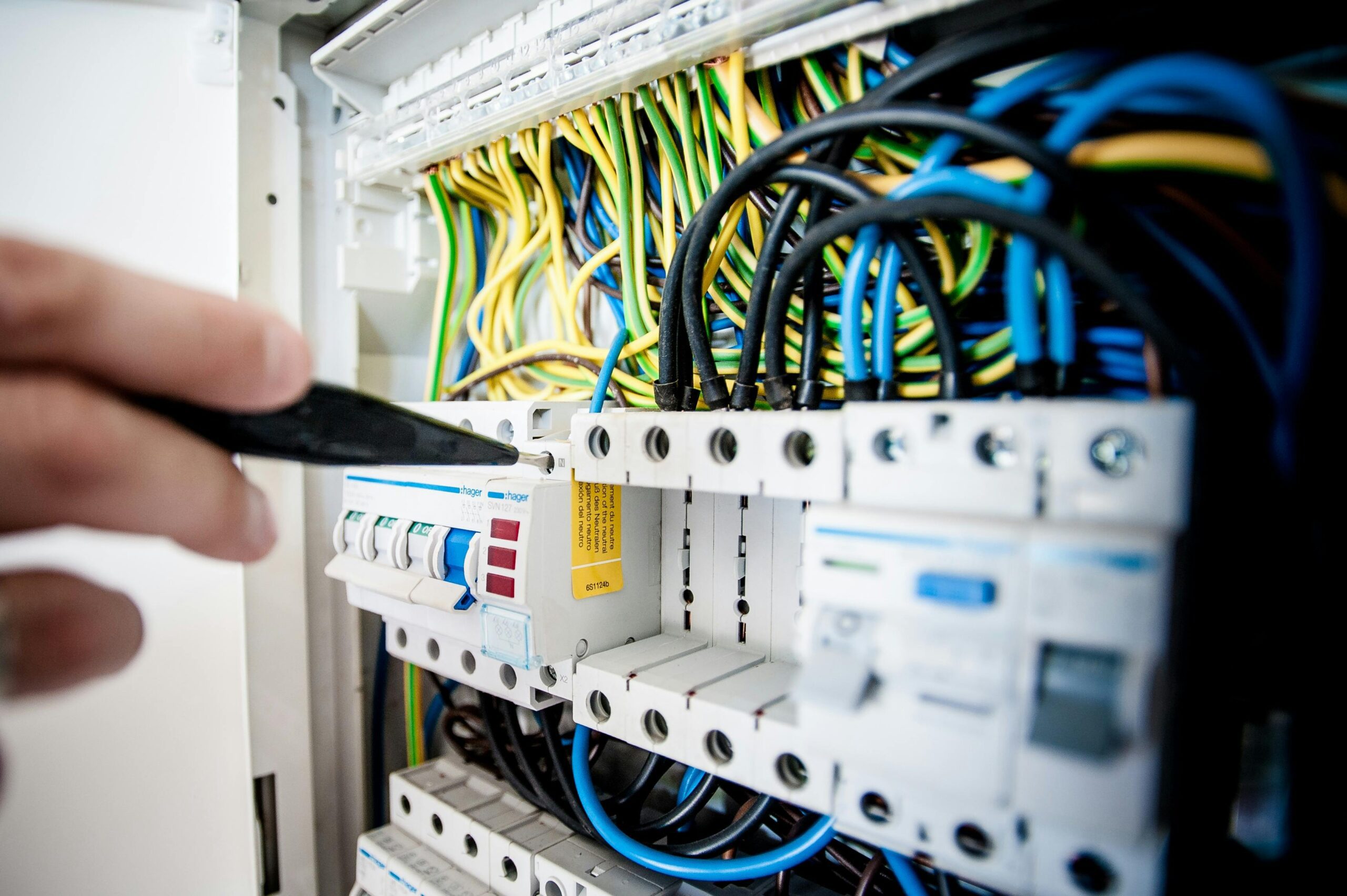 Strona główna Hand of electrician working on a circuit breaker panel with colorful wires, ensuring safe electrical connections.